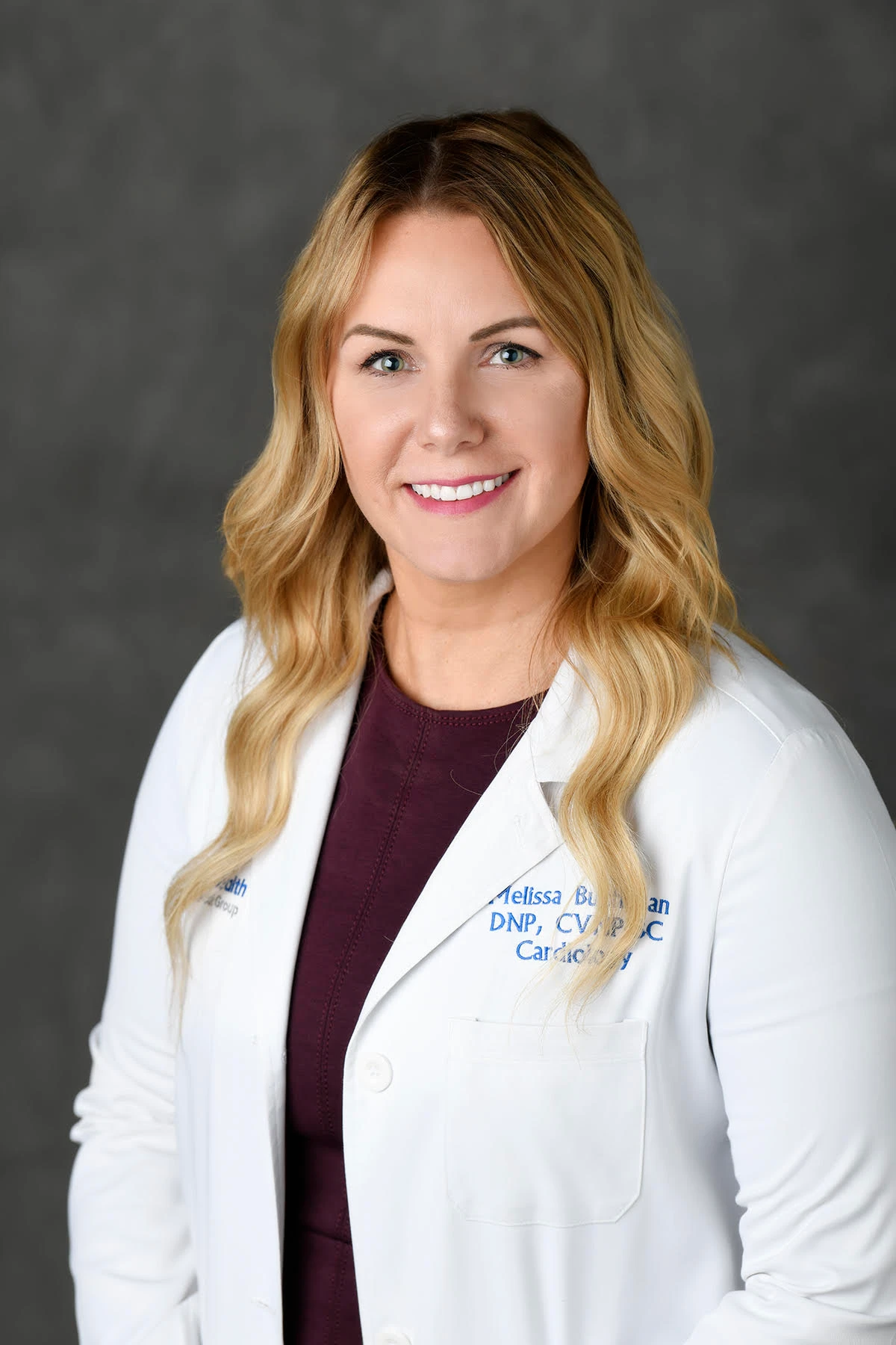 Melissa Buchanan, APRN, smiling in a white coat against a soft grey background
